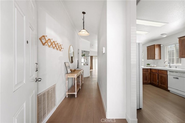 hall with a sink, wood finished floors, visible vents, and baseboards