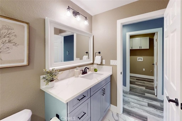 half bathroom featuring marble finish floor, toilet, vanity, and baseboards