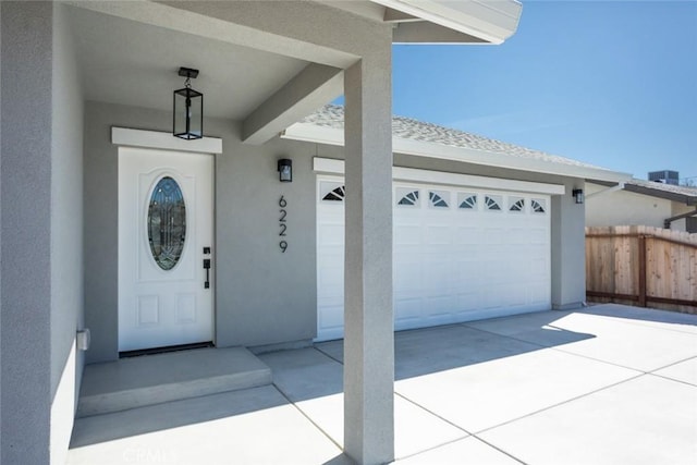 doorway to property featuring stucco siding, driveway, a garage, and fence