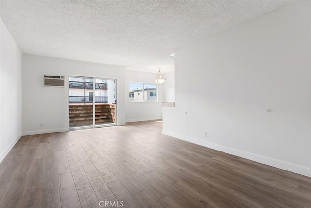 unfurnished living room featuring a textured ceiling, a wall mounted air conditioner, baseboards, and wood finished floors