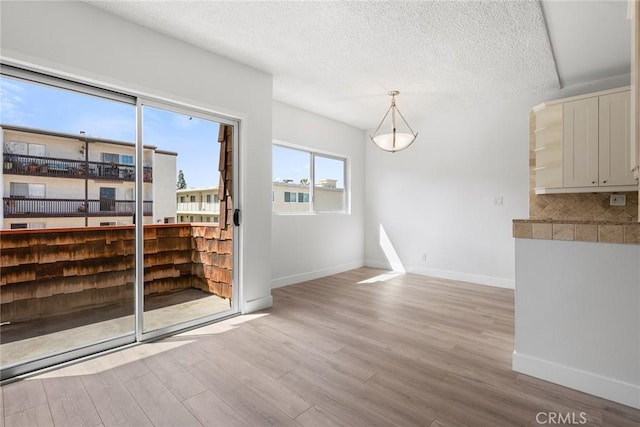 unfurnished dining area featuring wood finished floors, baseboards, and a textured ceiling