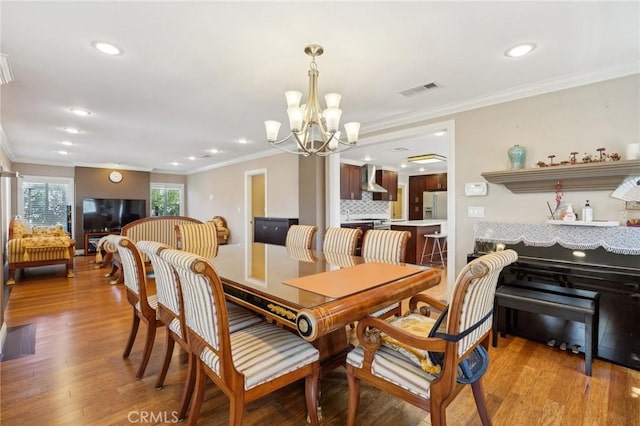 dining space featuring visible vents, an inviting chandelier, wood finished floors, and ornamental molding