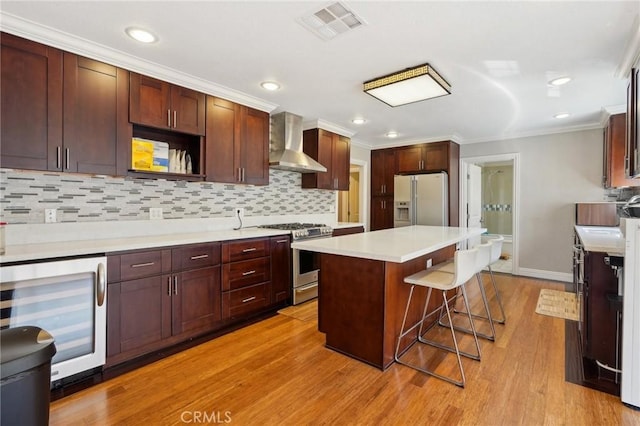 kitchen with beverage cooler, visible vents, white fridge with ice dispenser, wall chimney exhaust hood, and stainless steel gas stove