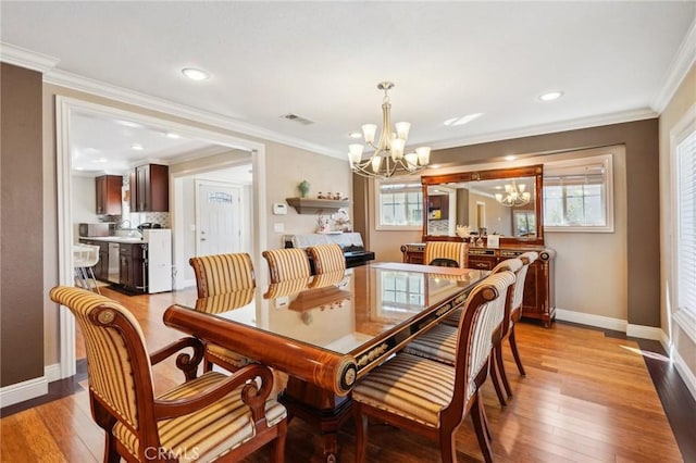 dining area featuring an inviting chandelier, light wood finished floors, baseboards, ornamental molding, and visible vents