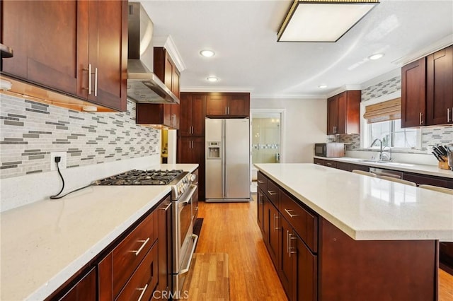 kitchen featuring fridge with ice dispenser, wall chimney range hood, crown molding, light wood finished floors, and high end range