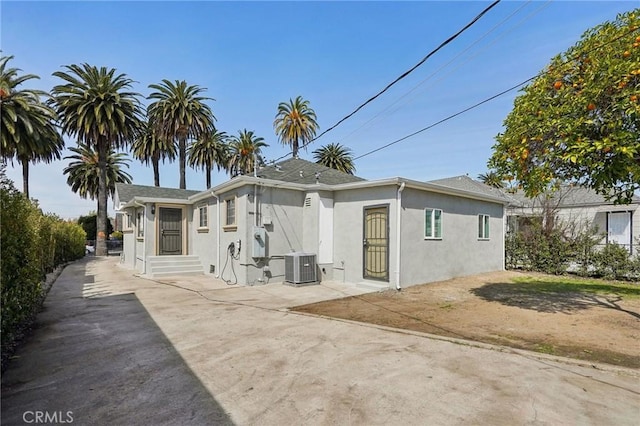 rear view of house featuring stucco siding, driveway, central air condition unit, and entry steps