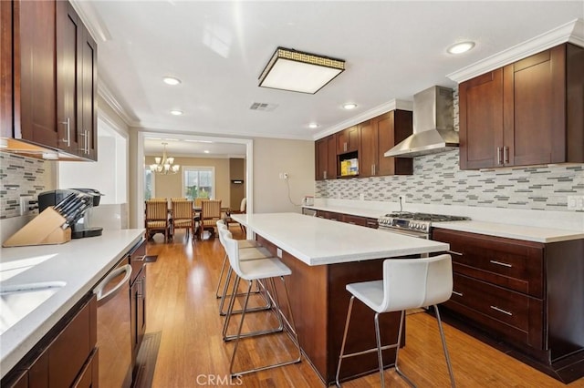 kitchen featuring visible vents, a breakfast bar area, appliances with stainless steel finishes, wood finished floors, and wall chimney exhaust hood