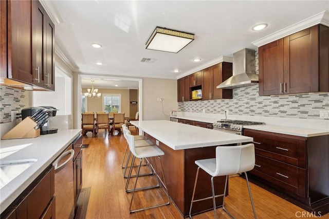 kitchen featuring a kitchen bar, tasteful backsplash, wall chimney range hood, and appliances with stainless steel finishes