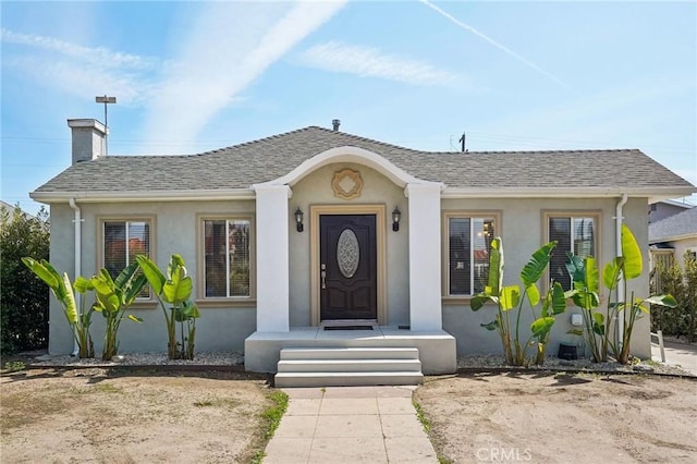 view of front of home with stucco siding, roof with shingles, and a chimney