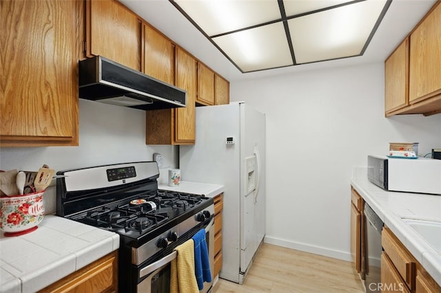 kitchen featuring under cabinet range hood, appliances with stainless steel finishes, light wood-style flooring, and tile countertops