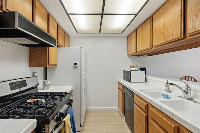 kitchen featuring extractor fan, tile counters, brown cabinetry, black appliances, and a sink