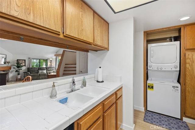 laundry room featuring laundry area, stacked washer and clothes dryer, light wood-style floors, and a sink