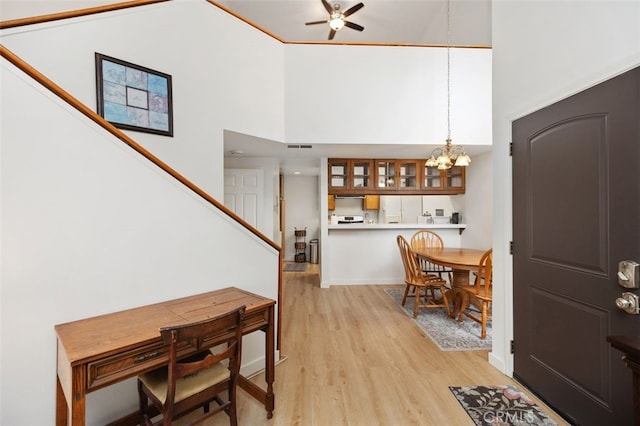 foyer featuring visible vents, stairway, ceiling fan with notable chandelier, light wood-style floors, and a towering ceiling