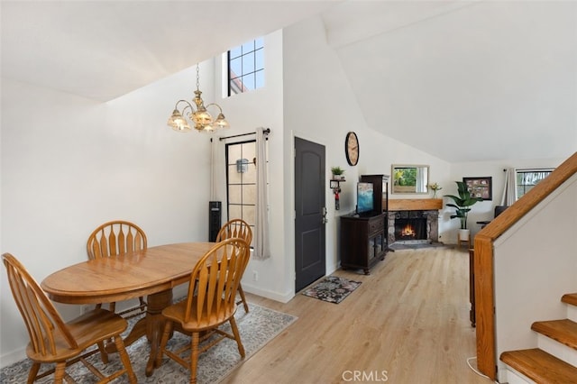 dining room featuring light wood finished floors, a high end fireplace, stairs, an inviting chandelier, and high vaulted ceiling