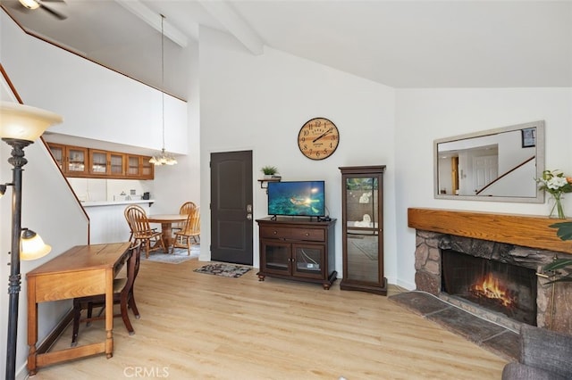 living room with beam ceiling, a notable chandelier, a stone fireplace, and light wood-style floors