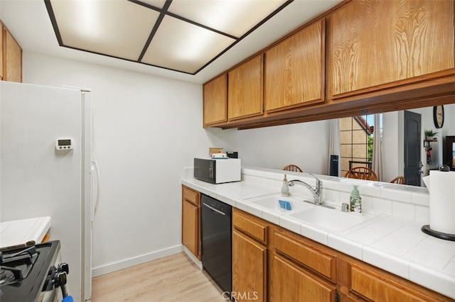 kitchen featuring brown cabinets, black appliances, a sink, light wood-style floors, and tile counters