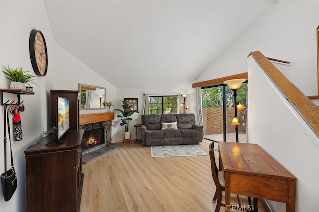 living area featuring light wood-style flooring, a warm lit fireplace, and lofted ceiling