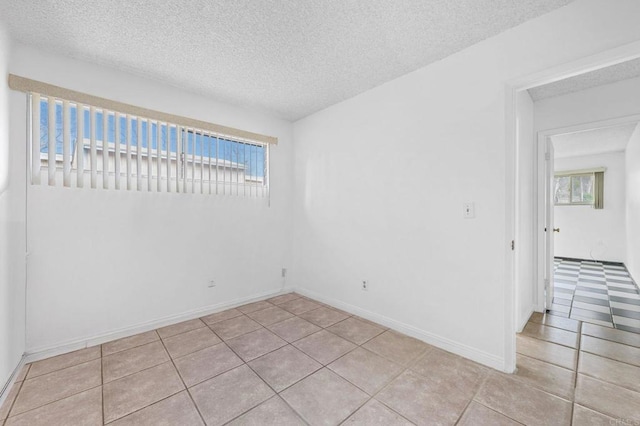 tiled spare room featuring a wealth of natural light, baseboards, and a textured ceiling