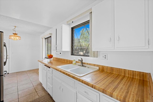 kitchen with baseboards, light tile patterned floors, freestanding refrigerator, white cabinets, and a sink