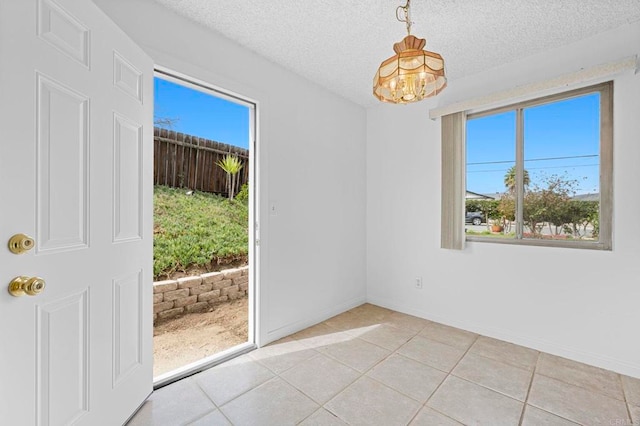 interior space featuring light tile patterned floors, a notable chandelier, a textured ceiling, and baseboards