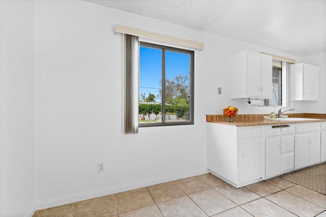 kitchen with a sink, a textured ceiling, white cabinets, light tile patterned floors, and baseboards