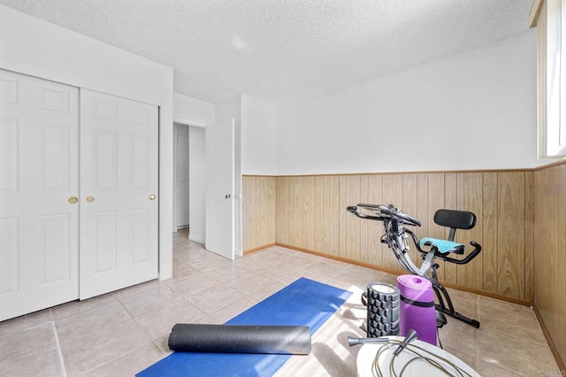 exercise area featuring a textured ceiling, light tile patterned floors, wood walls, and wainscoting