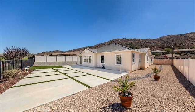 rear view of property featuring stucco siding, a tiled roof, a fenced backyard, a mountain view, and a patio area