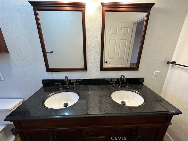 bathroom with a sink, toilet, and double vanity