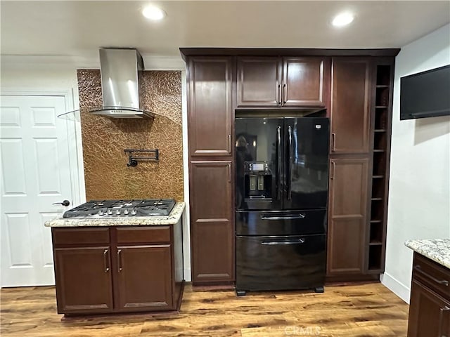 kitchen featuring tasteful backsplash, light wood-style floors, wall chimney exhaust hood, black refrigerator with ice dispenser, and stainless steel gas cooktop
