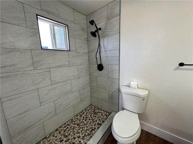 bathroom featuring baseboards, tiled shower, and toilet