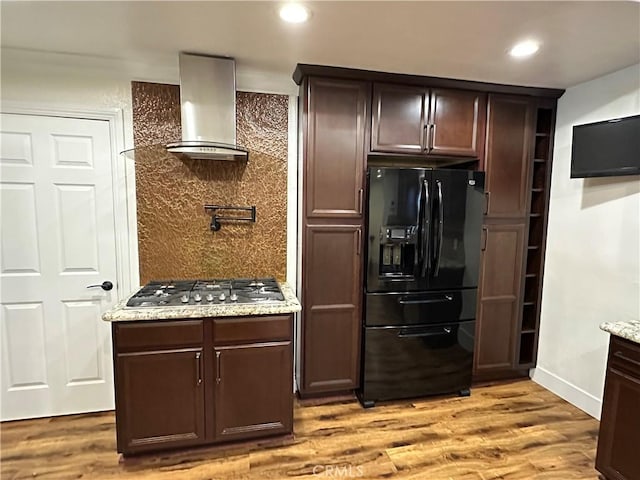 kitchen with black fridge, tasteful backsplash, light wood-style floors, stainless steel gas stovetop, and wall chimney range hood