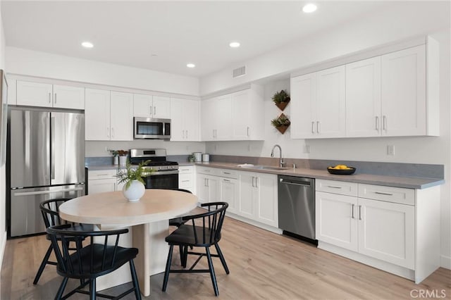 kitchen with a sink, light wood-style flooring, appliances with stainless steel finishes, and white cabinets