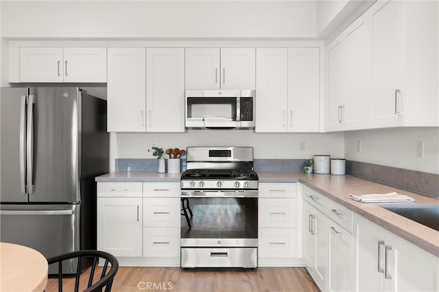 kitchen with light wood-type flooring, appliances with stainless steel finishes, light countertops, and white cabinetry