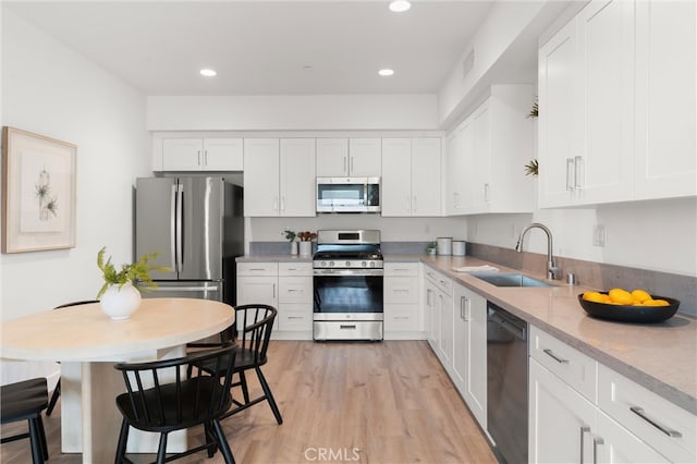 kitchen with a sink, stainless steel appliances, white cabinets, and light wood finished floors