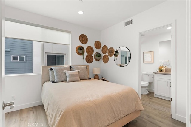 bedroom with light wood finished floors, visible vents, ensuite bath, and baseboards