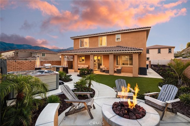 back of house at dusk featuring fence, a hot tub, an outdoor living space with a fire pit, stucco siding, and a patio area