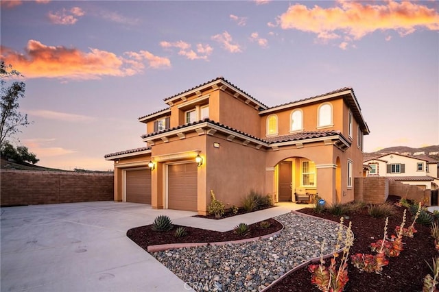 mediterranean / spanish house featuring stucco siding, driveway, a tile roof, fence, and a garage