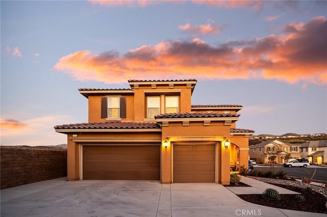 mediterranean / spanish-style home with stucco siding, concrete driveway, an attached garage, and a tiled roof