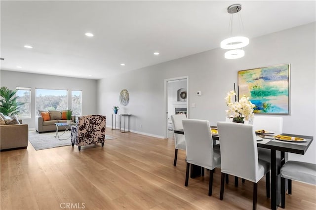 dining room with recessed lighting, light wood-type flooring, baseboards, and a warm lit fireplace