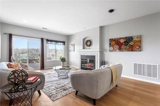 living area with visible vents, a tile fireplace, baseboards, and wood finished floors