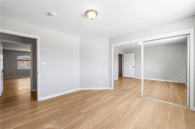 unfurnished bedroom with light wood-type flooring, baseboards, and a closet