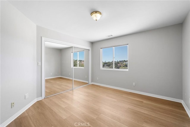 unfurnished bedroom featuring visible vents, baseboards, a closet, and light wood-style flooring