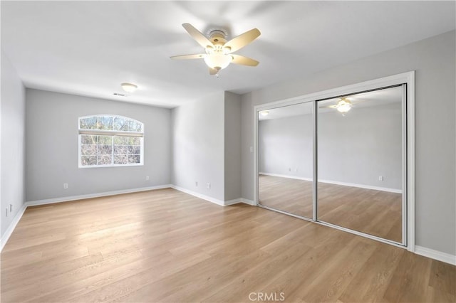 unfurnished bedroom with light wood finished floors, ceiling fan, a closet, and baseboards