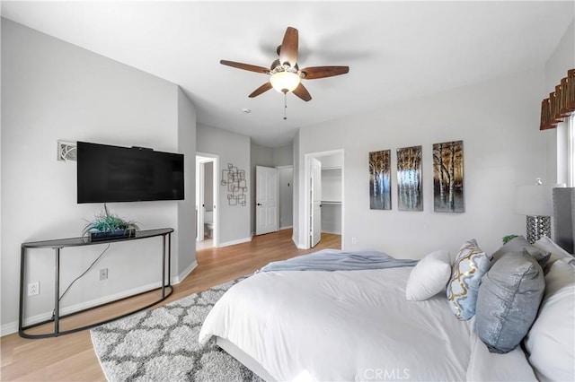 bedroom featuring light wood-style flooring, a spacious closet, baseboards, and ceiling fan