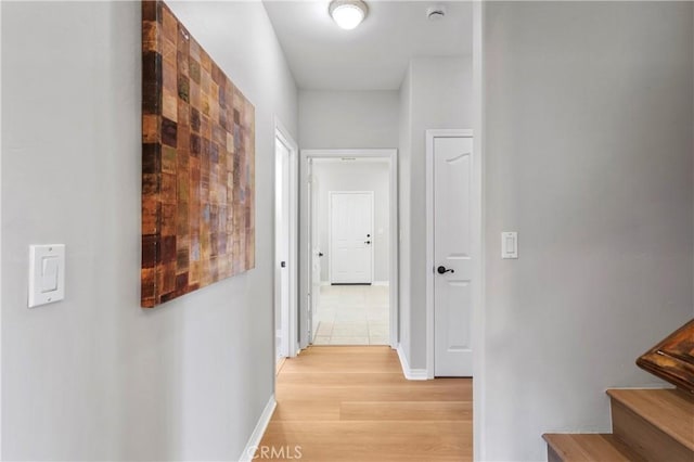 corridor with light wood finished floors, stairs, and baseboards