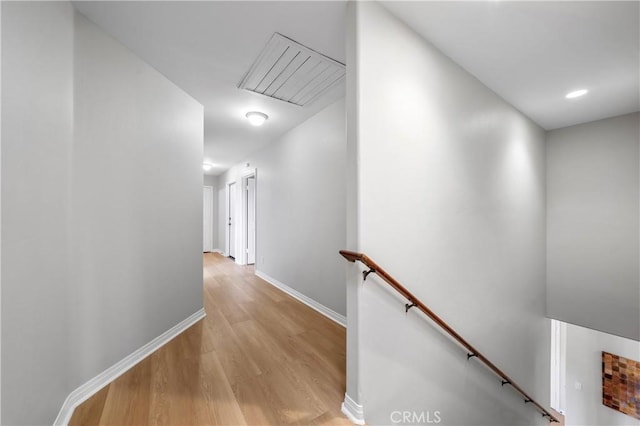 hall with an upstairs landing, baseboards, and light wood-style floors