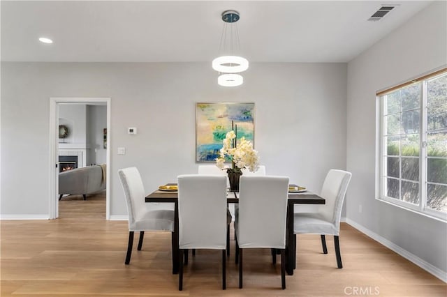 dining space with visible vents, baseboards, a warm lit fireplace, and light wood-style flooring