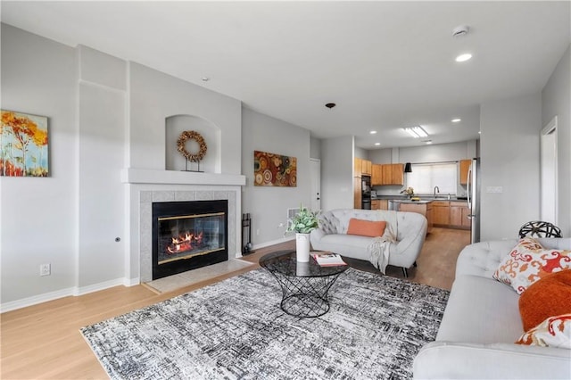 living room featuring recessed lighting, light wood-style flooring, a tile fireplace, and baseboards