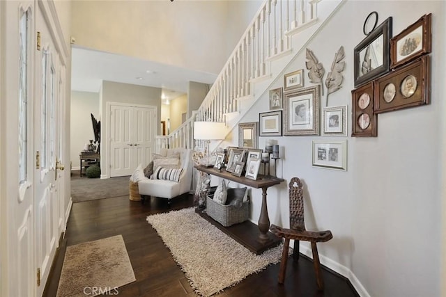 interior space with a high ceiling, stairs, dark wood-type flooring, and baseboards