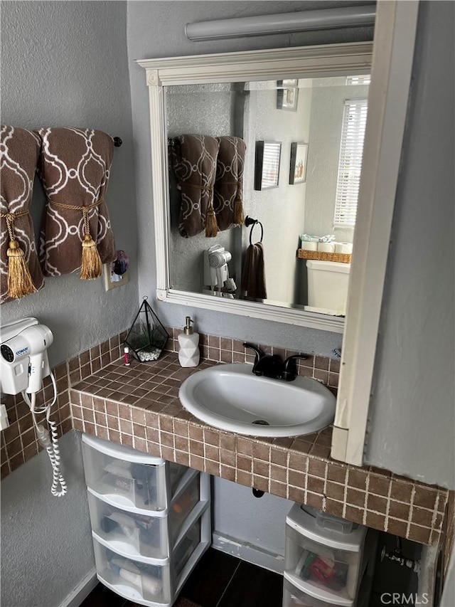 half bath featuring a textured wall and a sink